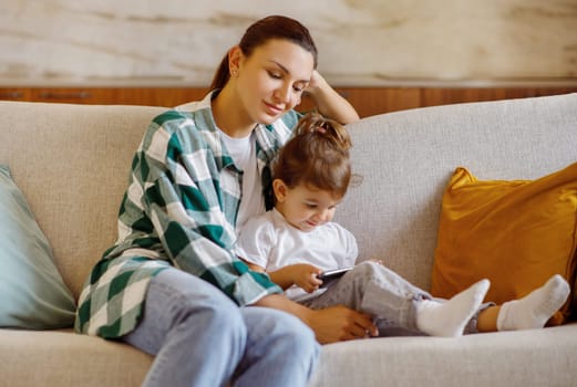 Mom and child relaxing with smartphone on cozy couch