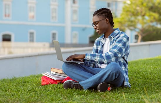black student guy typing on laptop having lecture at park