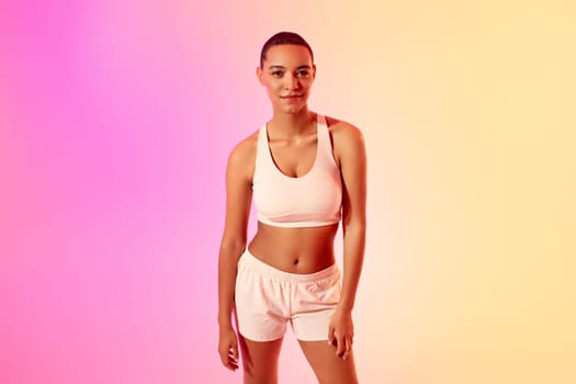 A confident young lady athlete with a short haircut poses in a sports bra and running shorts