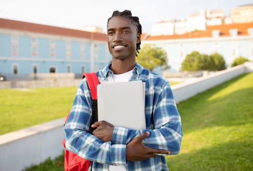 black student guy with backpack, laptop and workbooks posing outside