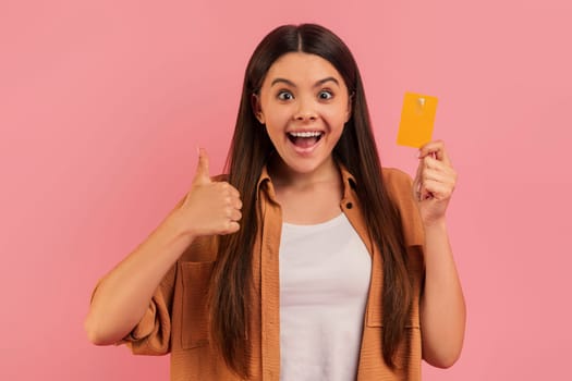 Ecstatic teenage girl holding credit card and giving thumb up