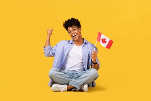 Joyful male student with Canadian flag cheering on yellow background