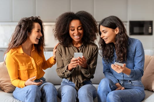 Three multiethnic women friends websurfing on cellphones in living room