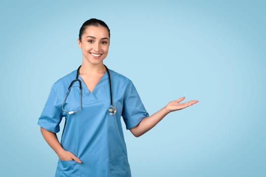 Confident female nurse presenting with hand in blue scrubs