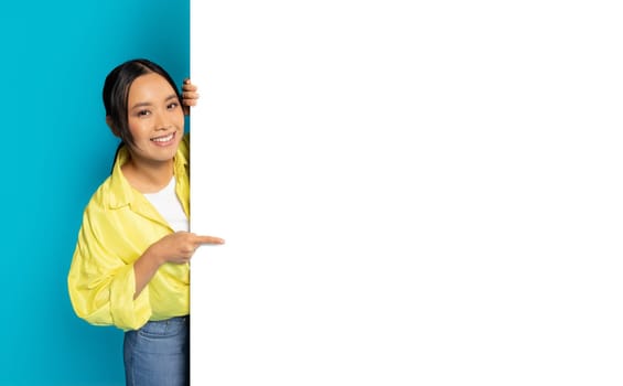 An Asian woman with a bright smile is peeking from behind a blank white vertical banner