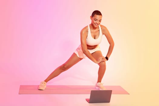 A focused woman with a shaved head stretches on a yoga mat in a side lunge position
