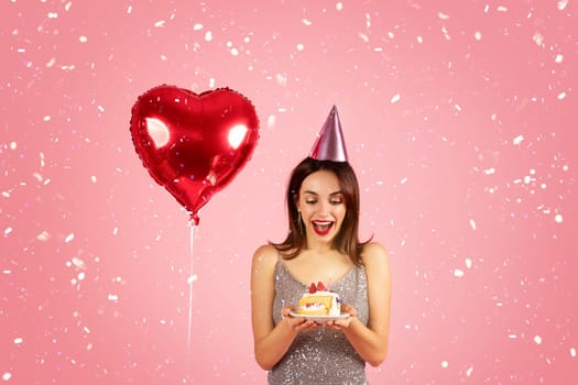 Delighted woman in a sequin dress with a party hat looking at a birthday cake