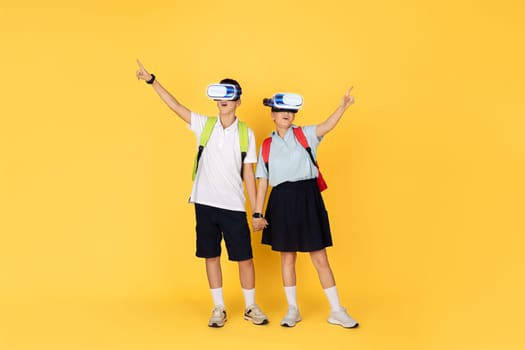 Two enthusiastic school students with backpacks hold hands while experiencing virtual reality