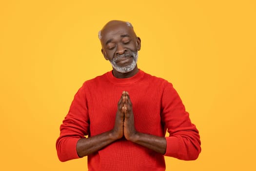 Peaceful senior Black man with a white beard in a meditative pose with hands together