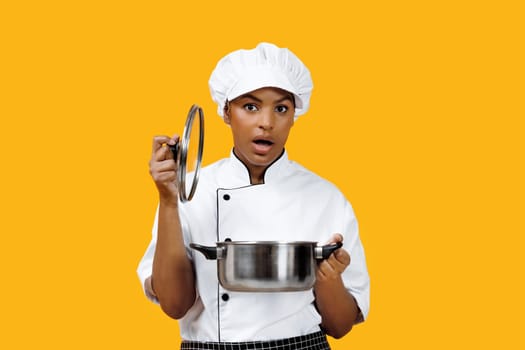 Surprised black female chef lifting lid off pot and looking at camera