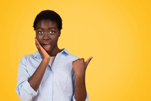 Glad shocked teen black lady student in casual with open mouth, point finger at empty space
