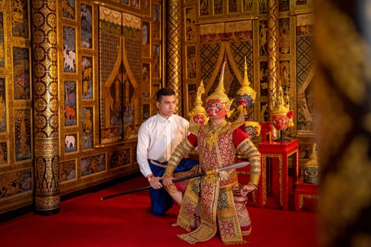 Side view of Asian man with Thai style cloth sit down with man wear ancient traditional Thai pattern Pantomime or Khon mask in traditional ceremony of respect to teacher.