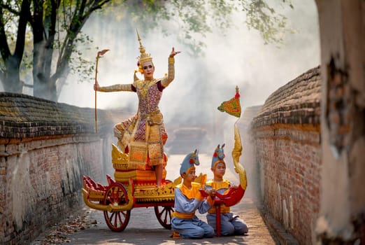 Asian man with old Thai traditional cloth hold weapon and stand and action of dance on traditional chariot also hold weapon stay in front of ancient building.