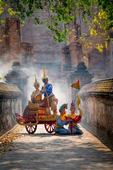 Vertical image of Khon Thai classic masked from the Ramakien with characters of woman and blue monkey stay together on traditional chariot in front of ancient building with mist or fog.