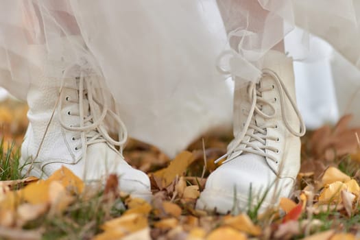 bride in white boots and dress is standing on fall leaves