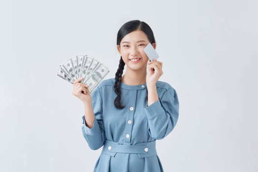 Young pretty asian woman wearing glasses shows a bank card and a fan of dollar bills