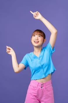 Feel the joy with a young Asian woman pointing to free copy space on purple background