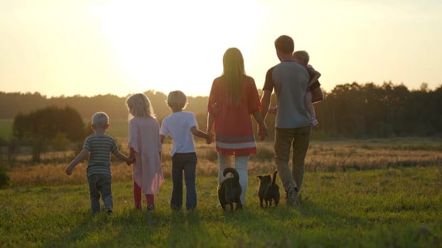 A large friendly family walks across the field at sunset.