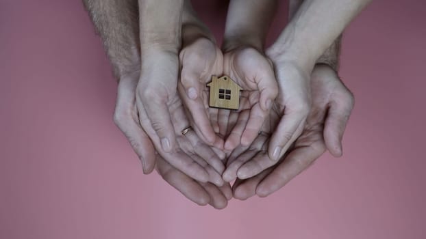 The concept of saving a friendly family. The hands of the mother and father with the child hold the figure in the form of a house.