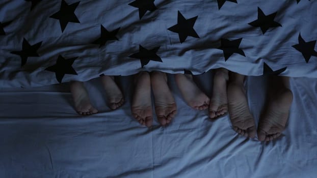 Legs of babies in the bed from under the covers before going to bed