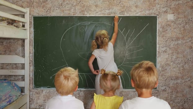 A six year old girl draws on a board in front of her sisters and brothers.