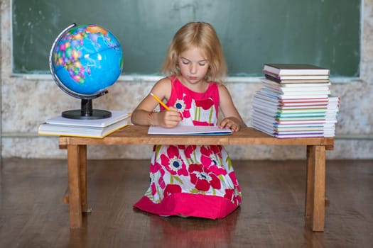 Little girl teaches home lessons on a bench against the background of the globe and books.