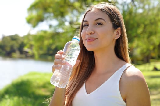 Attractive fitness woman looking away holding a bottle of water to drink in city park
