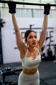 Asian sport woman stand and hanging bar look like relax after exercise in fitness gym with happiness.