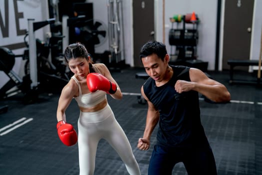 Asian sport trainer man help woman to practice with boxing for good action and movement in fitness gym.