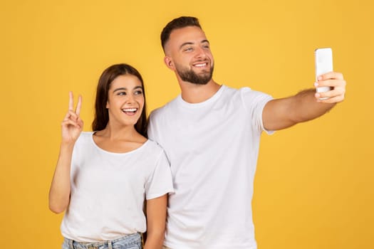A beaming young woman flashes a peace sign while taking a selfie with a smiling man