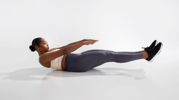 Determined young black woman performing V sit exercise, white background