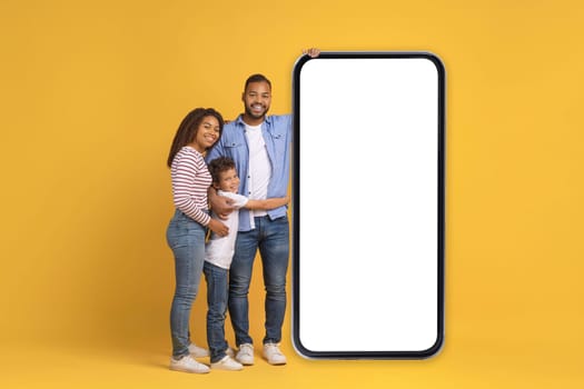 Happy Black Family Of Three Posing Near Blank Smartphone With White Screen