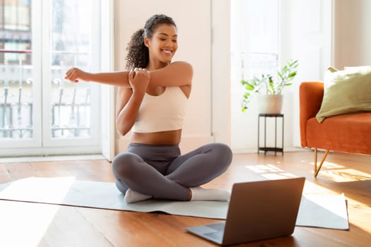 Lady looking at laptop during online workout stretching arm indoor