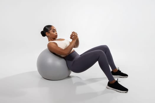 african woman doing abs exercises on fitness ball, white backdrop