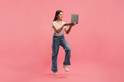 Active teenage girl holding an open laptop and jumping in air,