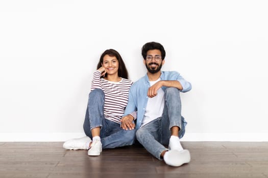 Hindu couple sitting on floor over white blank wall background