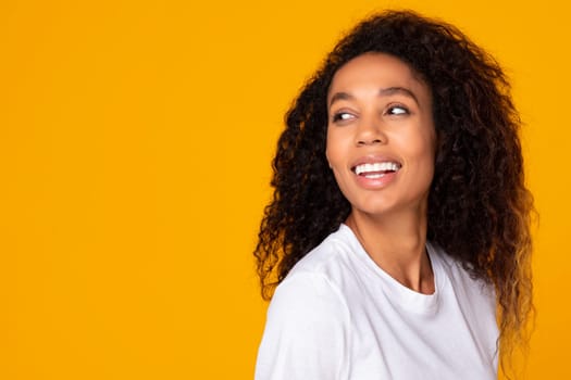 Black woman with curly hair on yellow backdrop looking aside