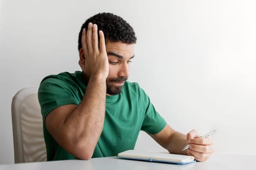 Frustrated man with a beard in a green t-shirt holding his head with one hand