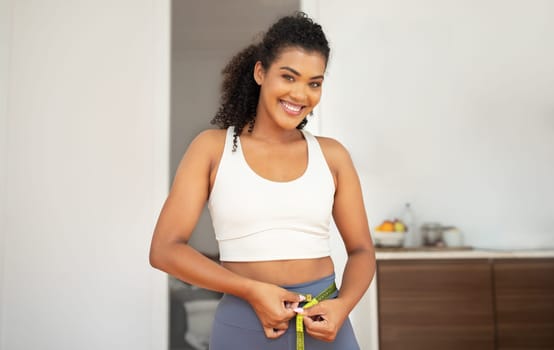 Athletic young woman measuring waist smiling to camera at home