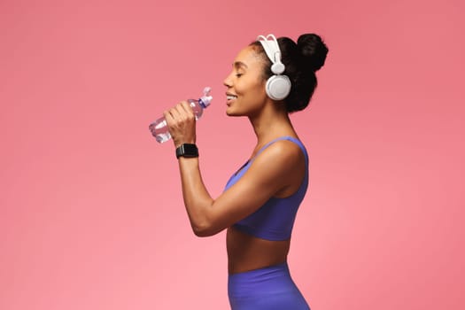 black lady enjoying water after workout on pink studio backdrop