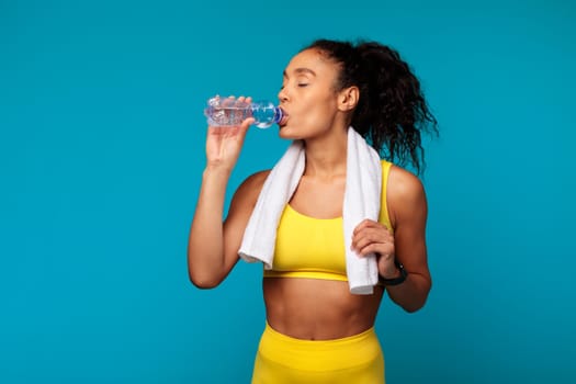 Fit black woman in sportswear sipping water from bottle, studio
