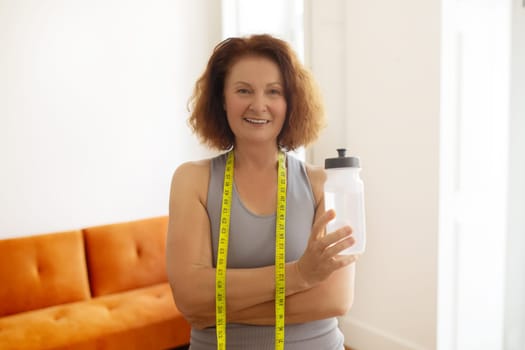 Smiling senior woman with tape measure around her neck holding water bottle