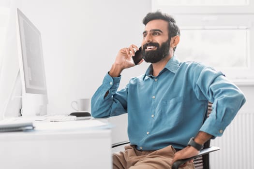 Cheerful indian businessman chatting on phone at his desk