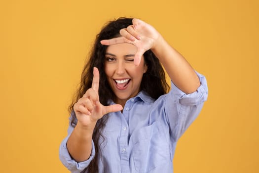 Enthusiastic young woman with curly hair making a frame with her hands