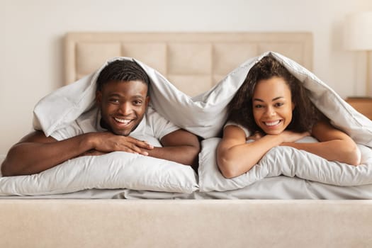 Happy Black Man And Woman Lying Under Blanket In Bed