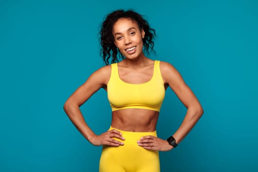african fitness lady in yellow sportswear smiling over blue background