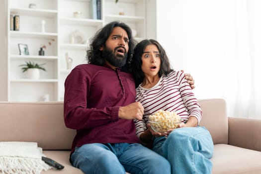 Shocked millennial indian couple watching horror movie on TV