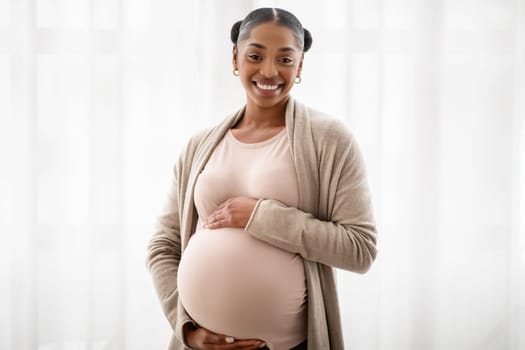 Happy black pregnant woman standing near window at home
