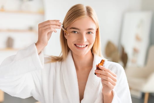 Blonde lady applies facial serum using dropper in bathroom