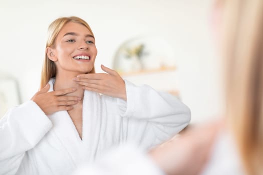 woman applies moisturizer to neck and face skin in bathroom